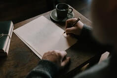 Человек за столом пишет ручкой на белом листе бумаги